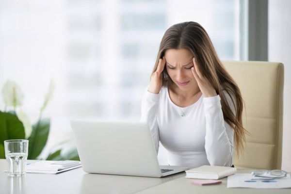 Stressed woman at computer suffering from a tension headache